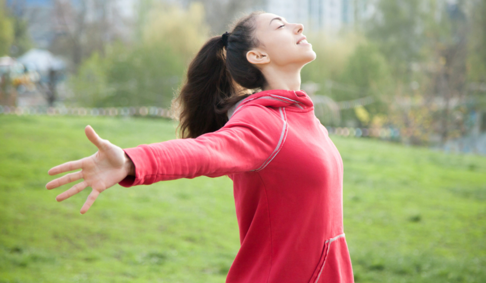 Profile portrait of happy sporty woman relaxing in park. Joyful female model relaxing, breathing fresh air outdoors with opened arms. Healthy active lifestyle concept